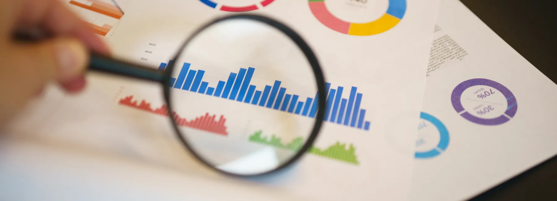 A hand looking at graphs with a magnifying glass