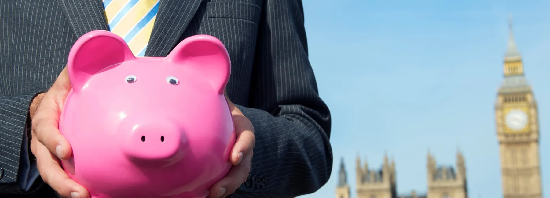a man in a suit holding a piggy bank in front of the houses of parliament