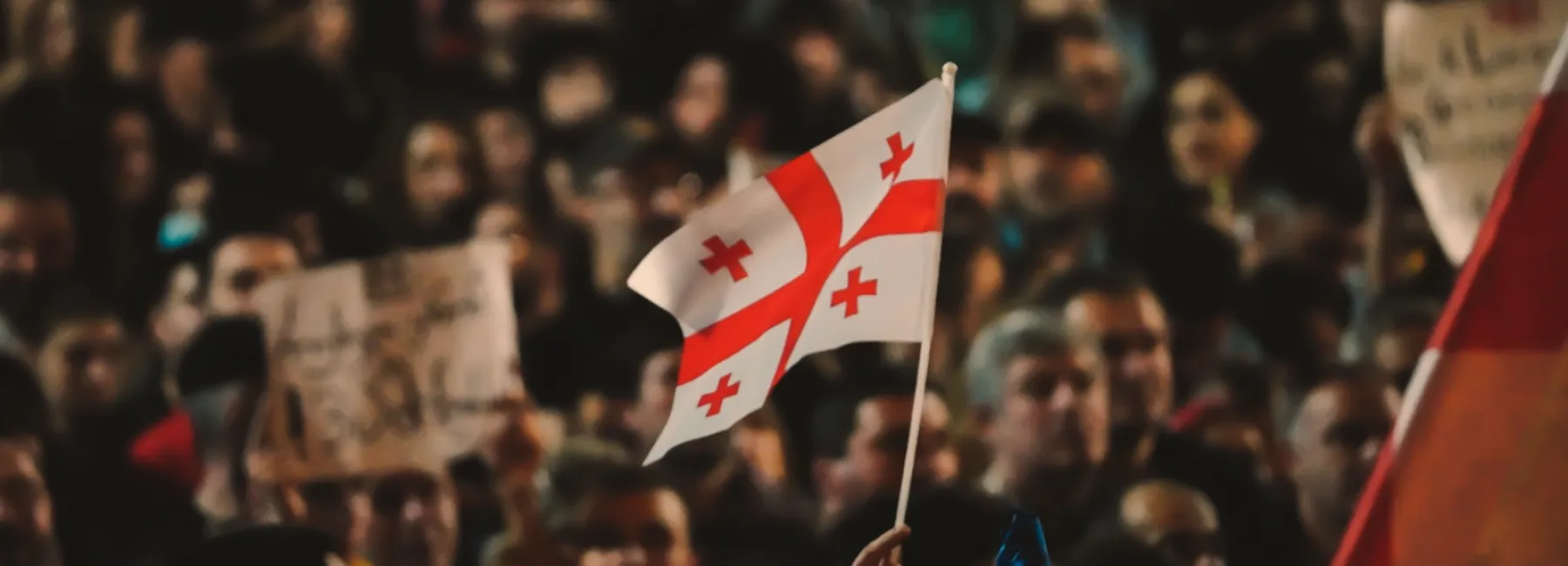 Small Georgian flag flies in front of a crowd of people