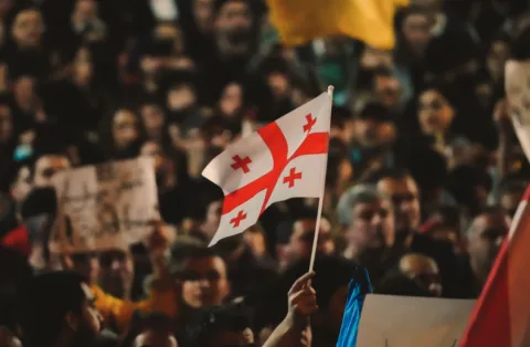 A small Georgian flag flies in front of a crowd of people