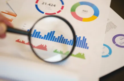 A hand looking at graphs with a magnifying glass
