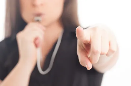 A woman pointing and blowing a whistle